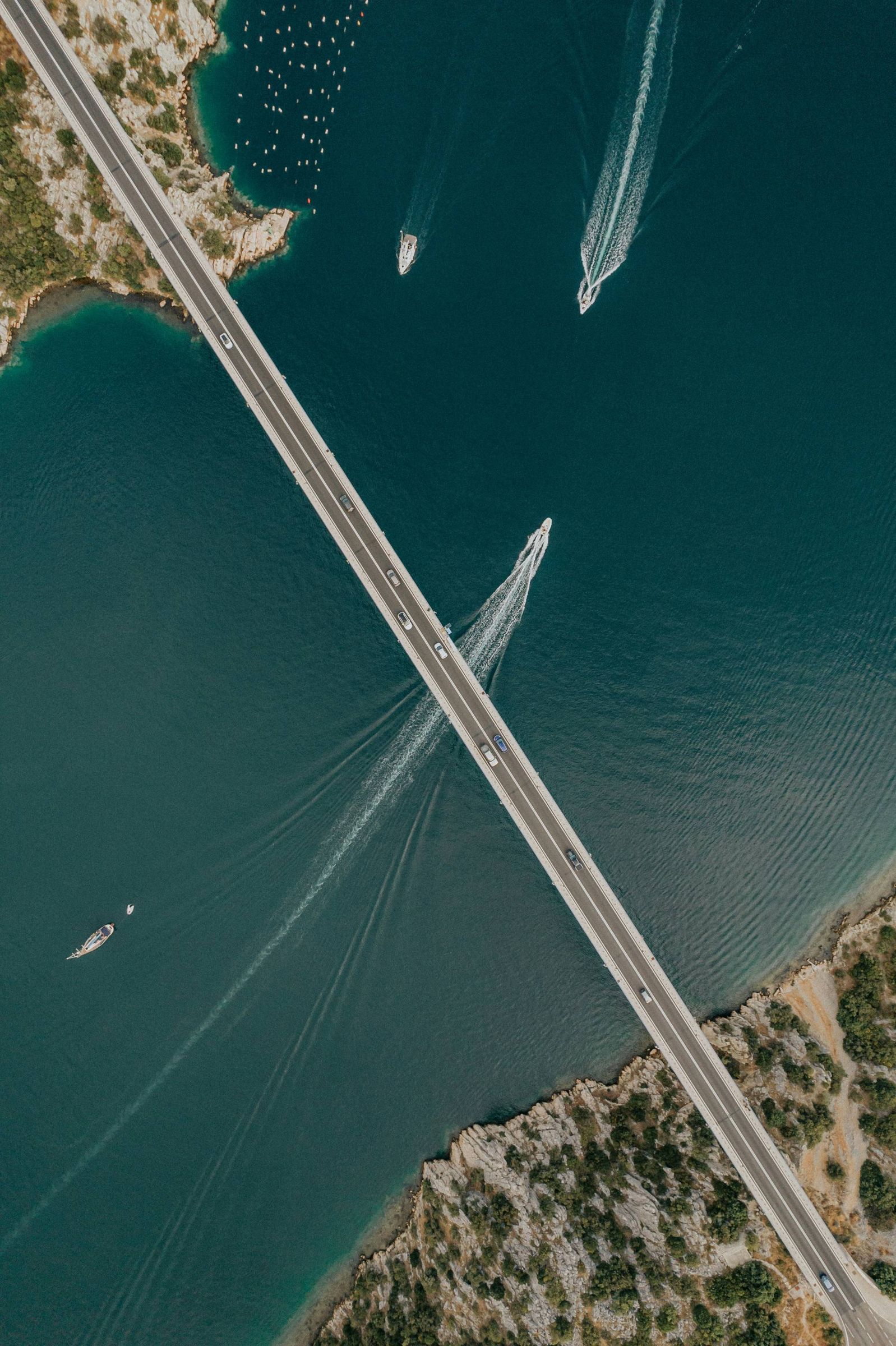 Aerial view of a long bridge crossing turquoise sea between two rocky coastlines