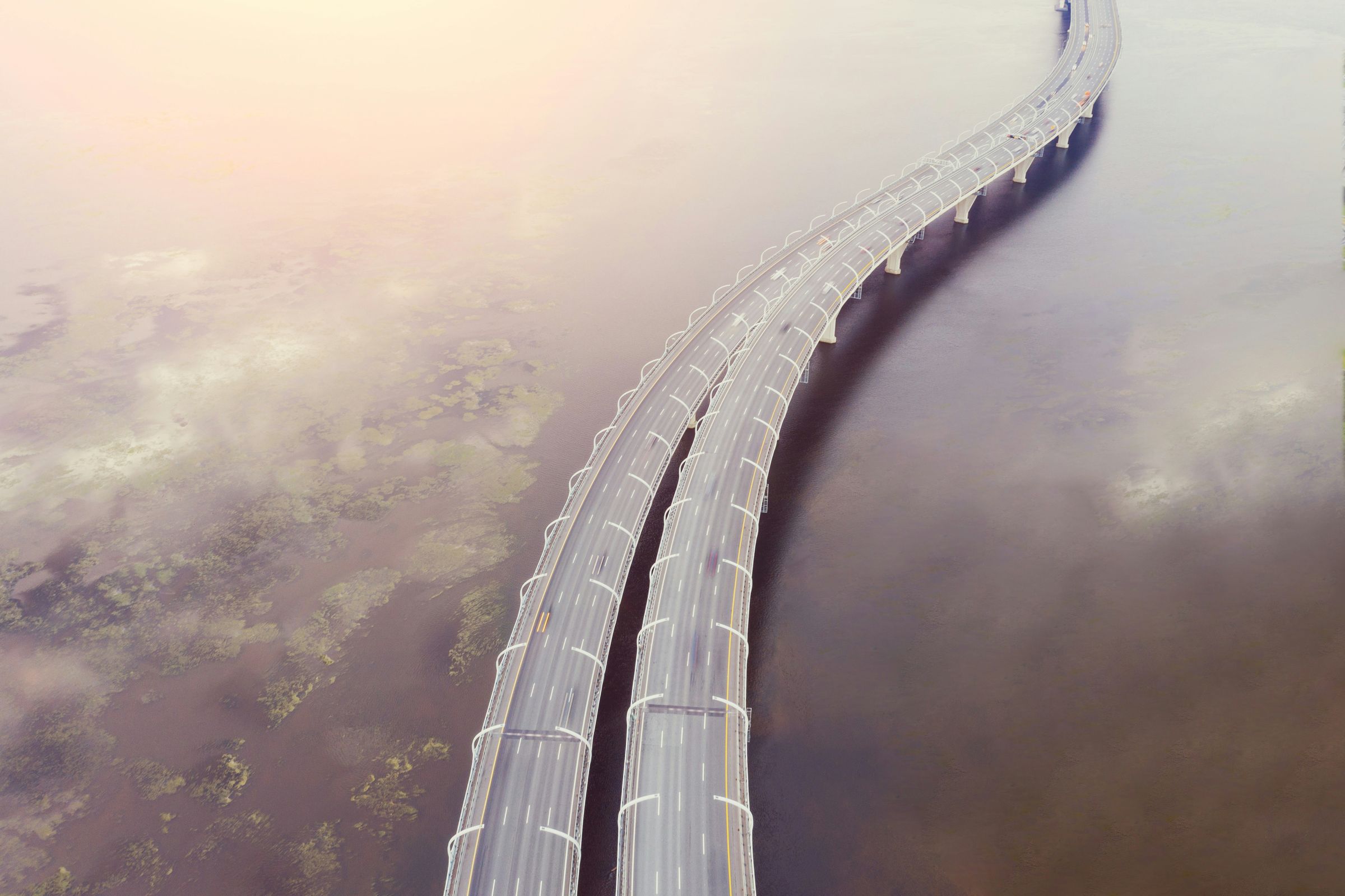 Curving highway bridge stretching across water in soft morning haze