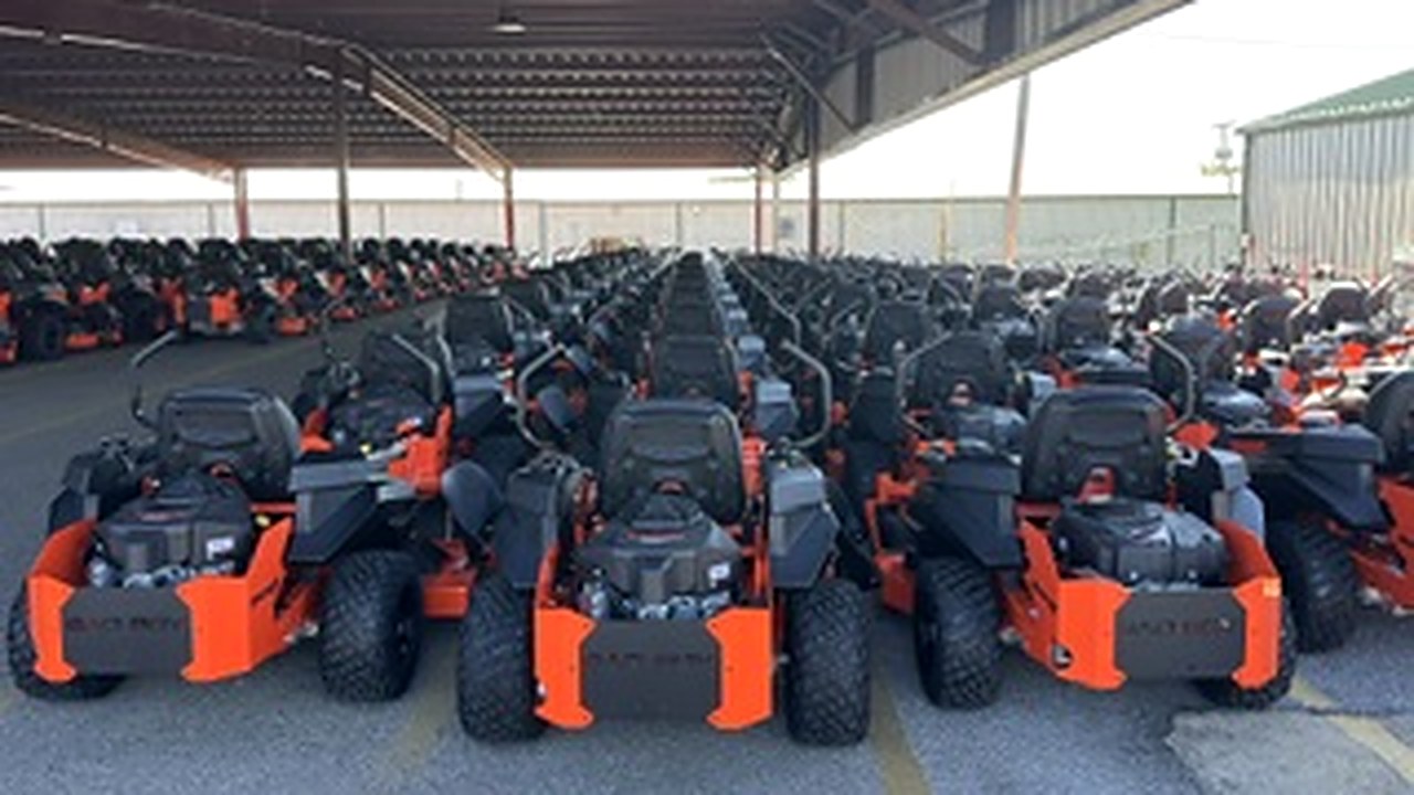 Rows of orange zero-turn mowers lined up under a covered canopy