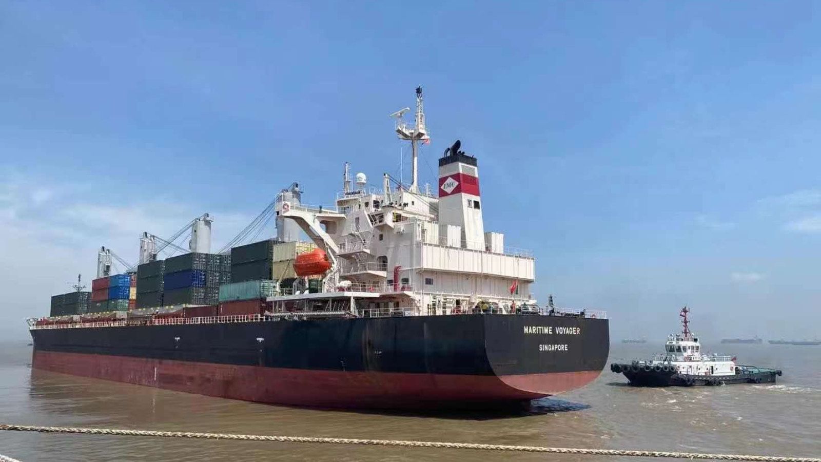 A container ship with a tug alongside in open water