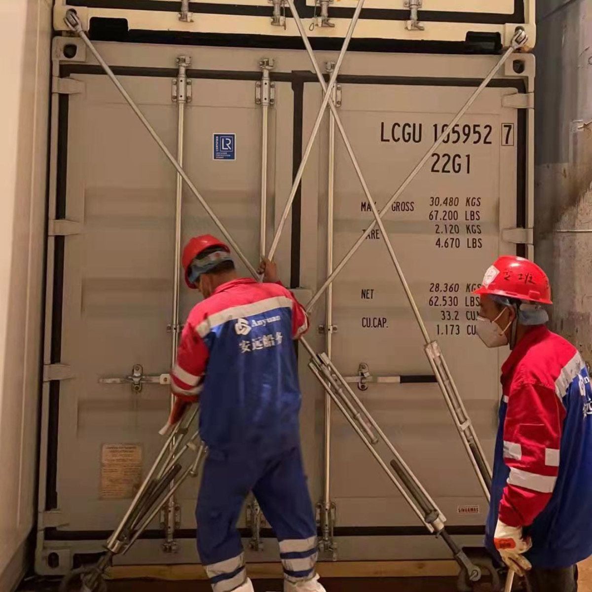 Port workers in hard hats securing the doors of a container