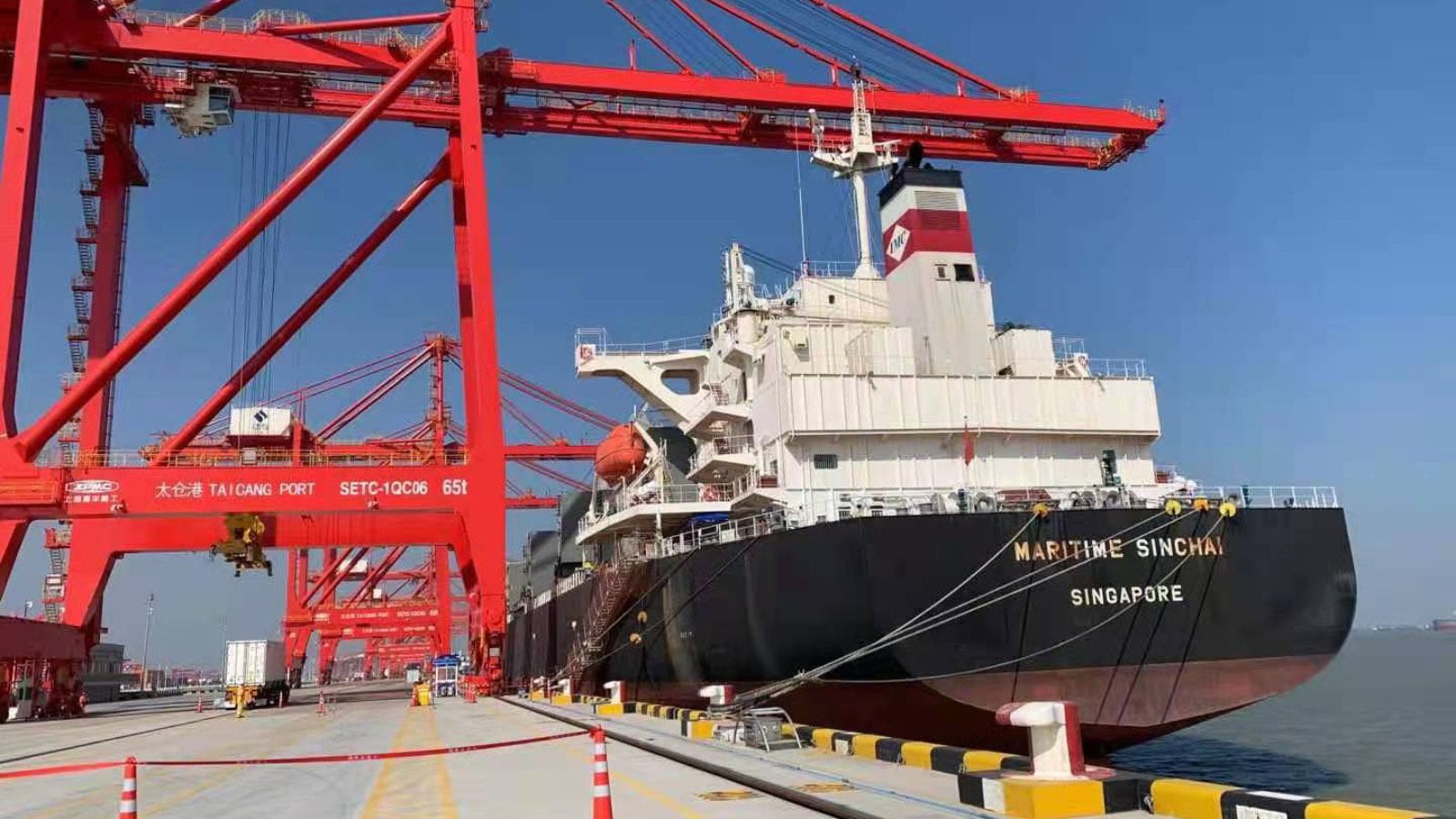 A container ship moored under red gantry cranes