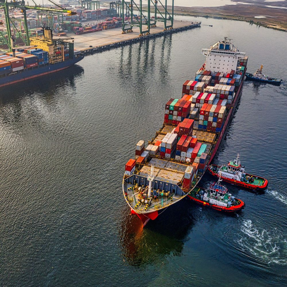 Aerial view of a loaded container ship guided by tugs at a port