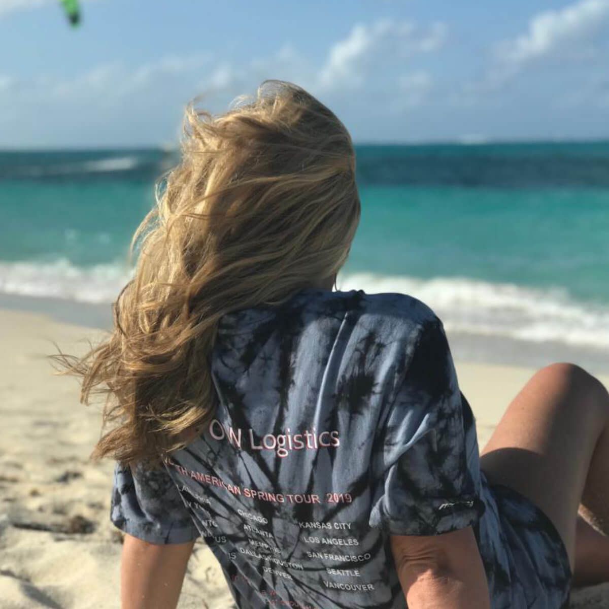 A woman in an OW Logistics tour T-shirt sitting on a beach