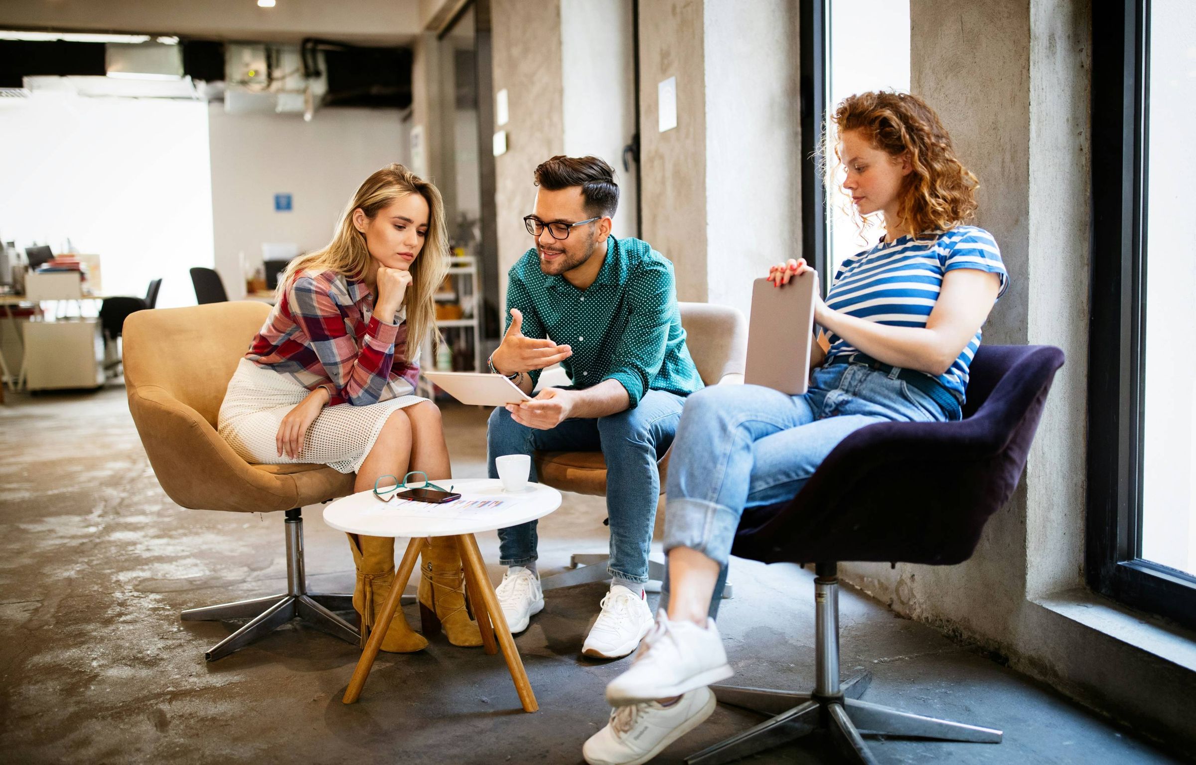 Three colleagues talking in armchairs in a bright office lounge