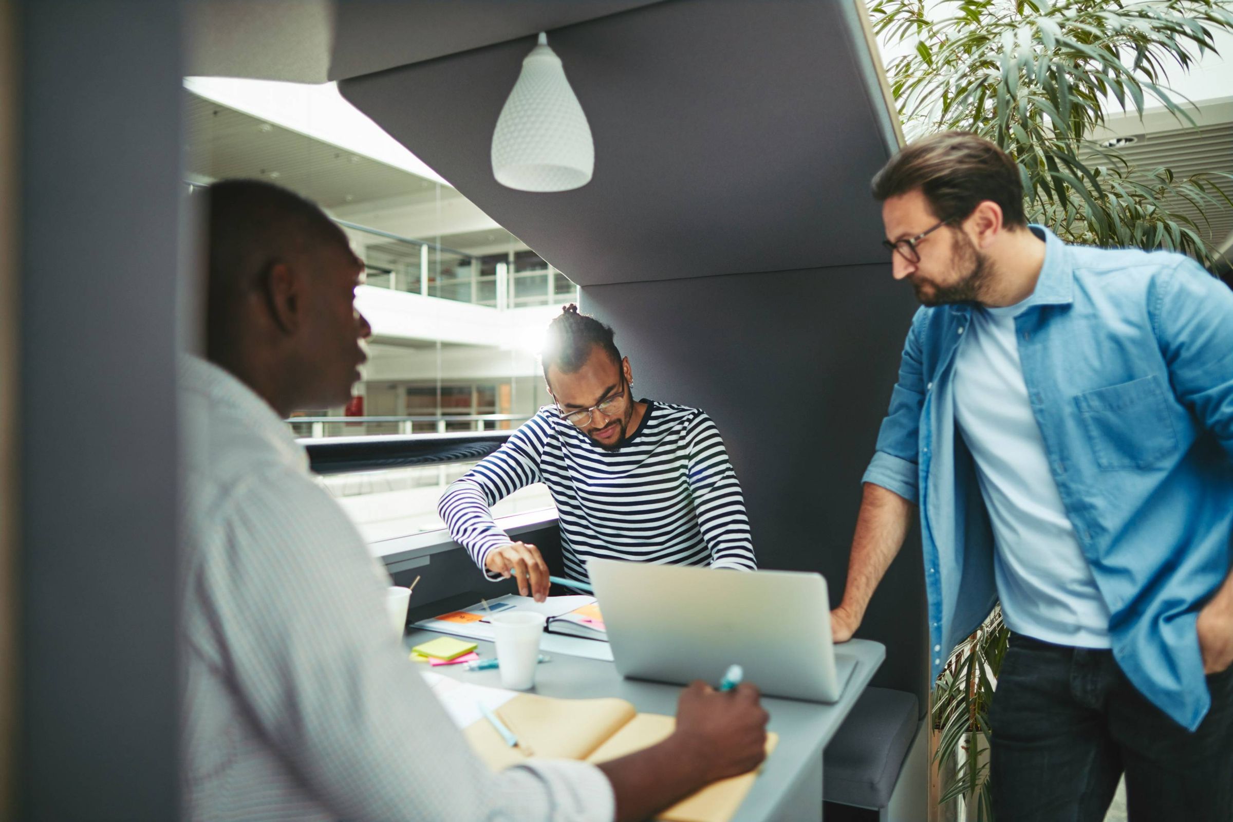 Three colleagues gathered around a laptop in an office meeting pod