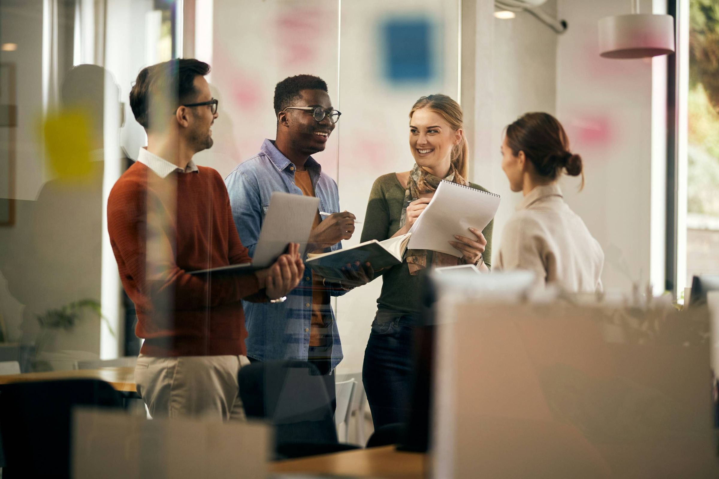 A team standing together, discussing notes and a laptop in a meeting room
