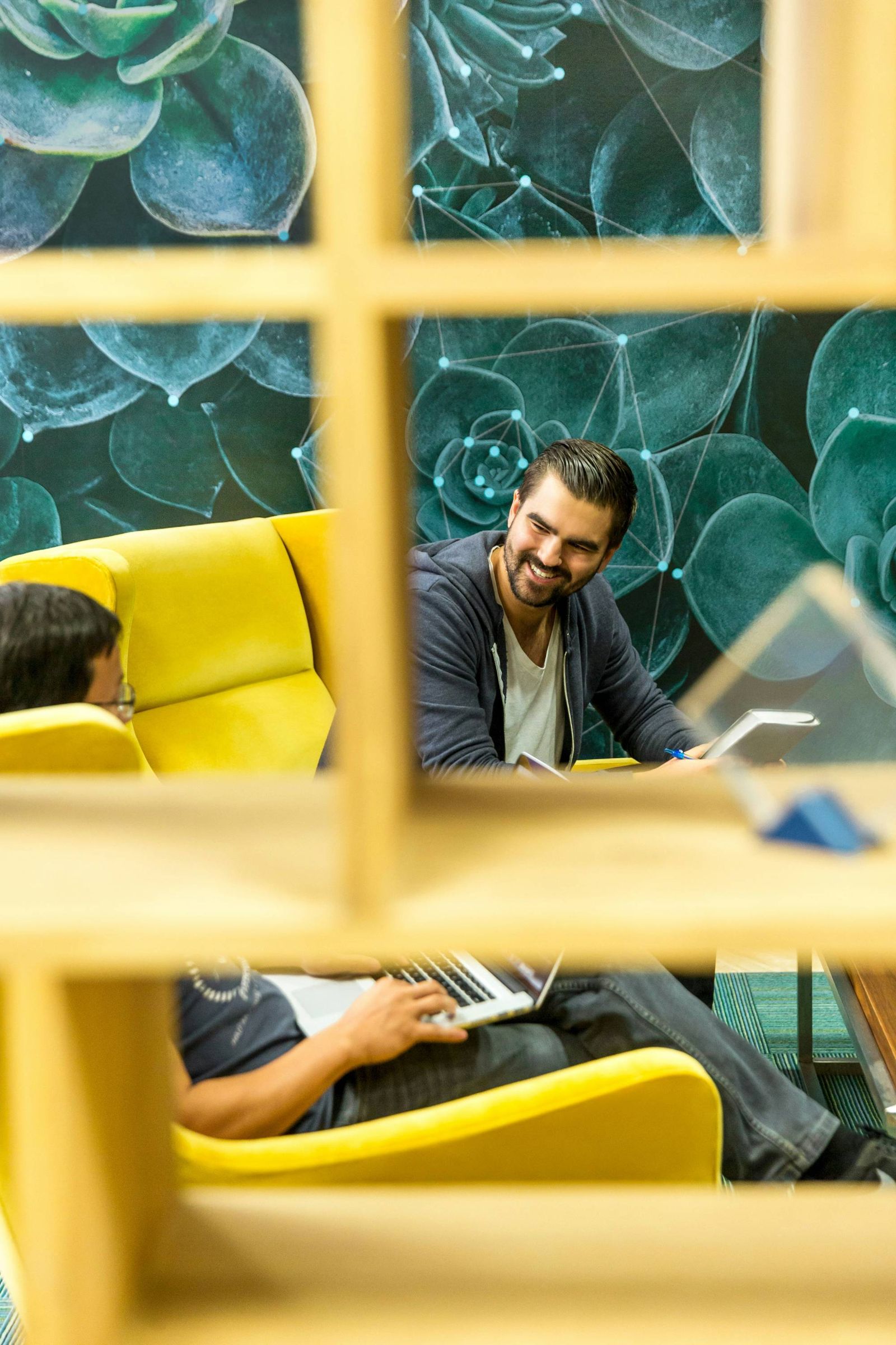A man working on a laptop in a yellow armchair, framed by shelving