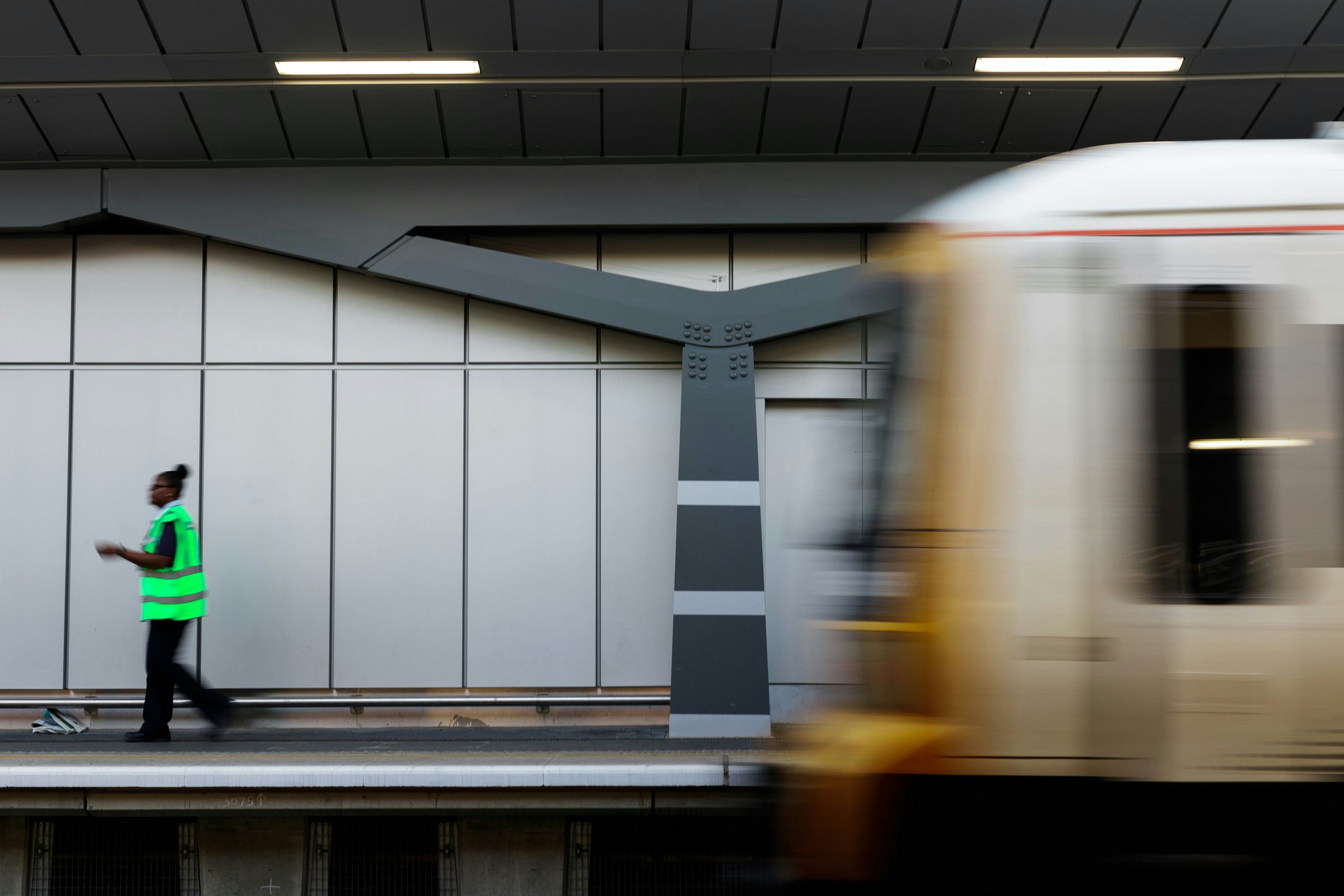 A worker in a high-visibility vest walking past a train speeding through a station