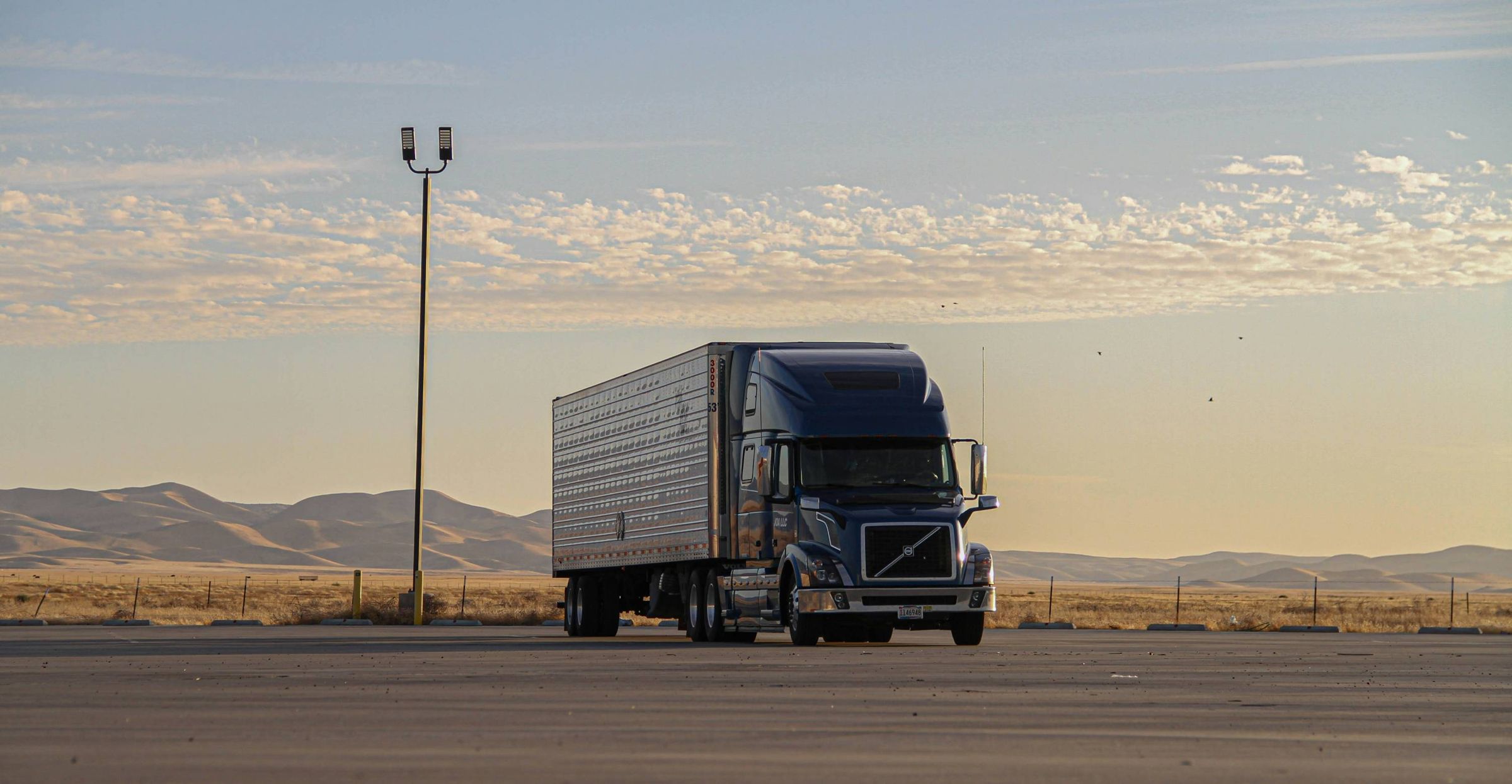 A blue semi-truck parked on a desert highway under an evening sky