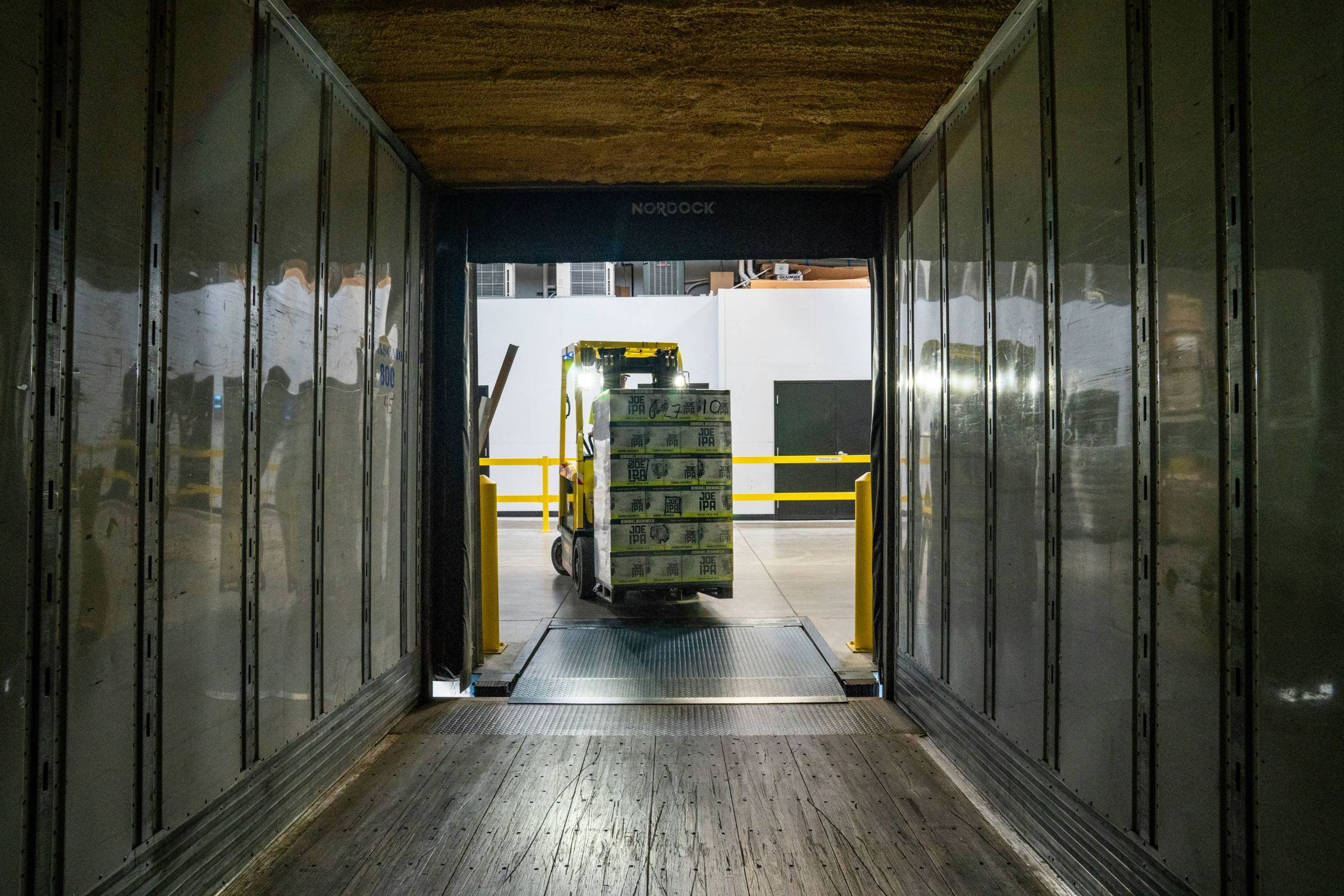 View from inside a trailer as a forklift loads a pallet at a warehouse dock