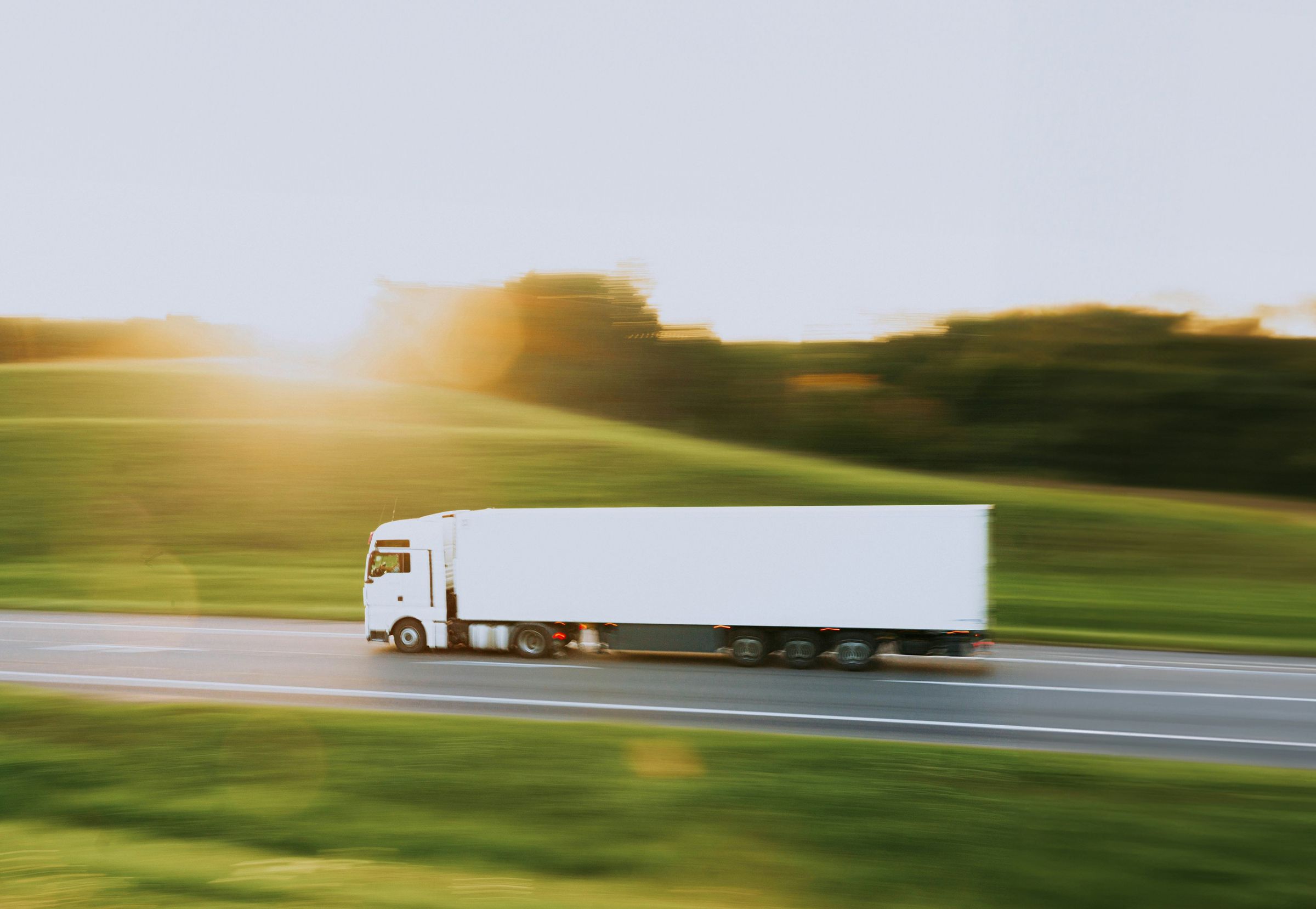 A white truck speeding along a highway past green fields at sunrise