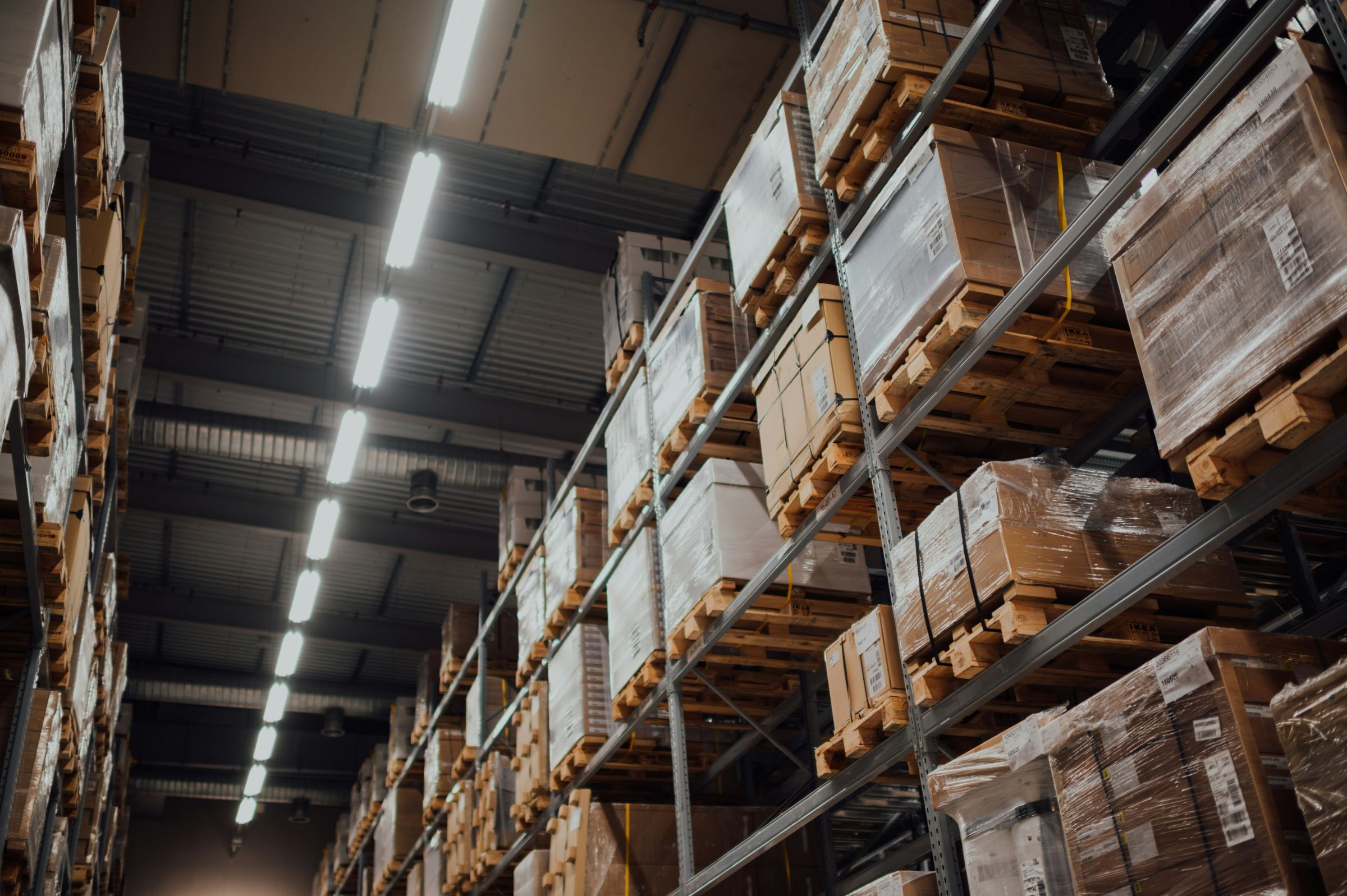 Warehouse racking stacked with wrapped pallets under long strip lights